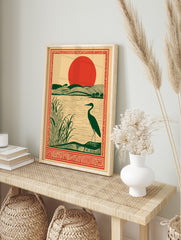 Illustrative art print of a dark green heron by a lake with reeds, rolling green hills, and a, in an alternate framed mockup