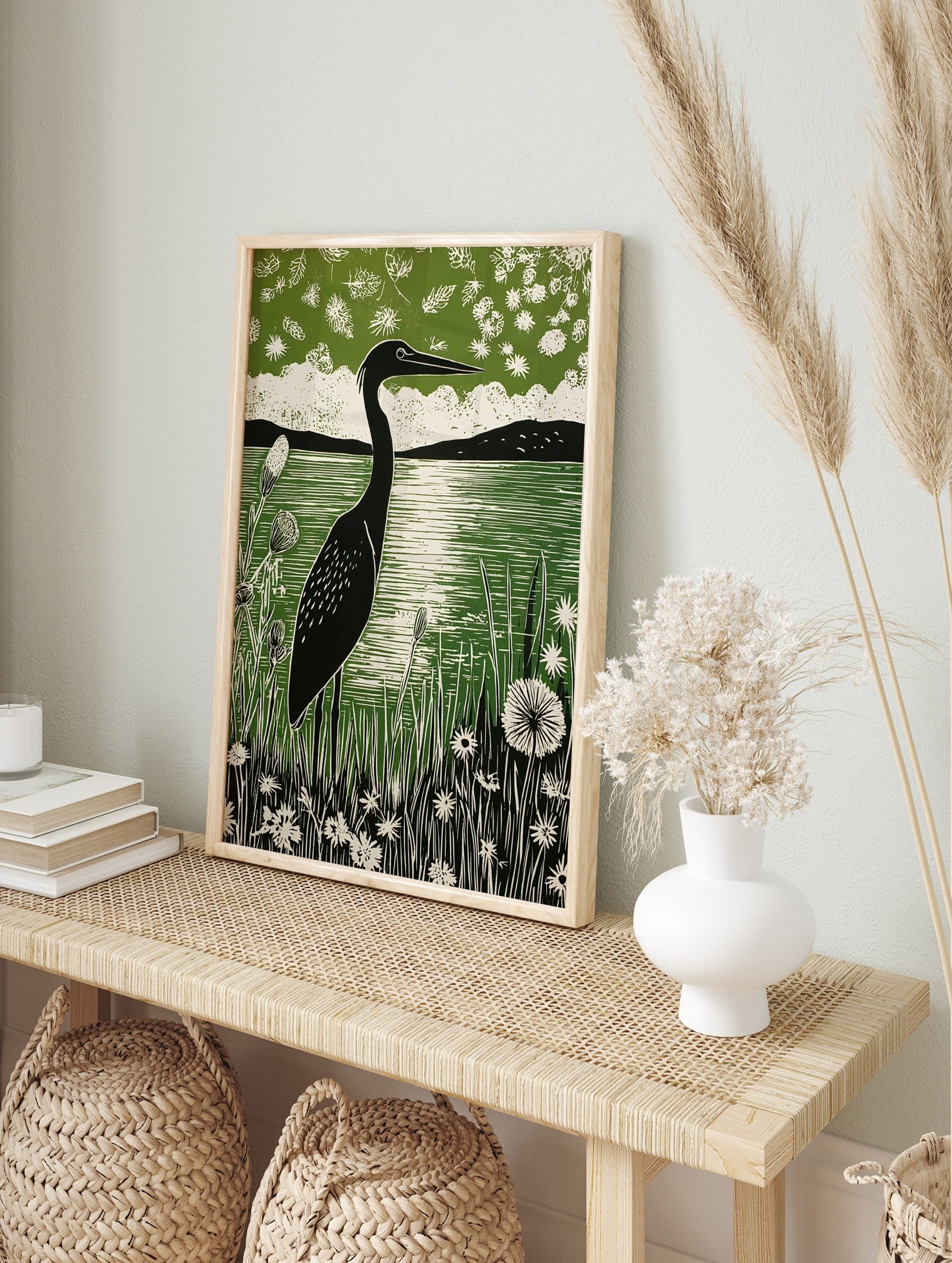 Linocut print of a black heron by a green lake, surrounded by white wildflowers and distant, in an alternate framed mockup