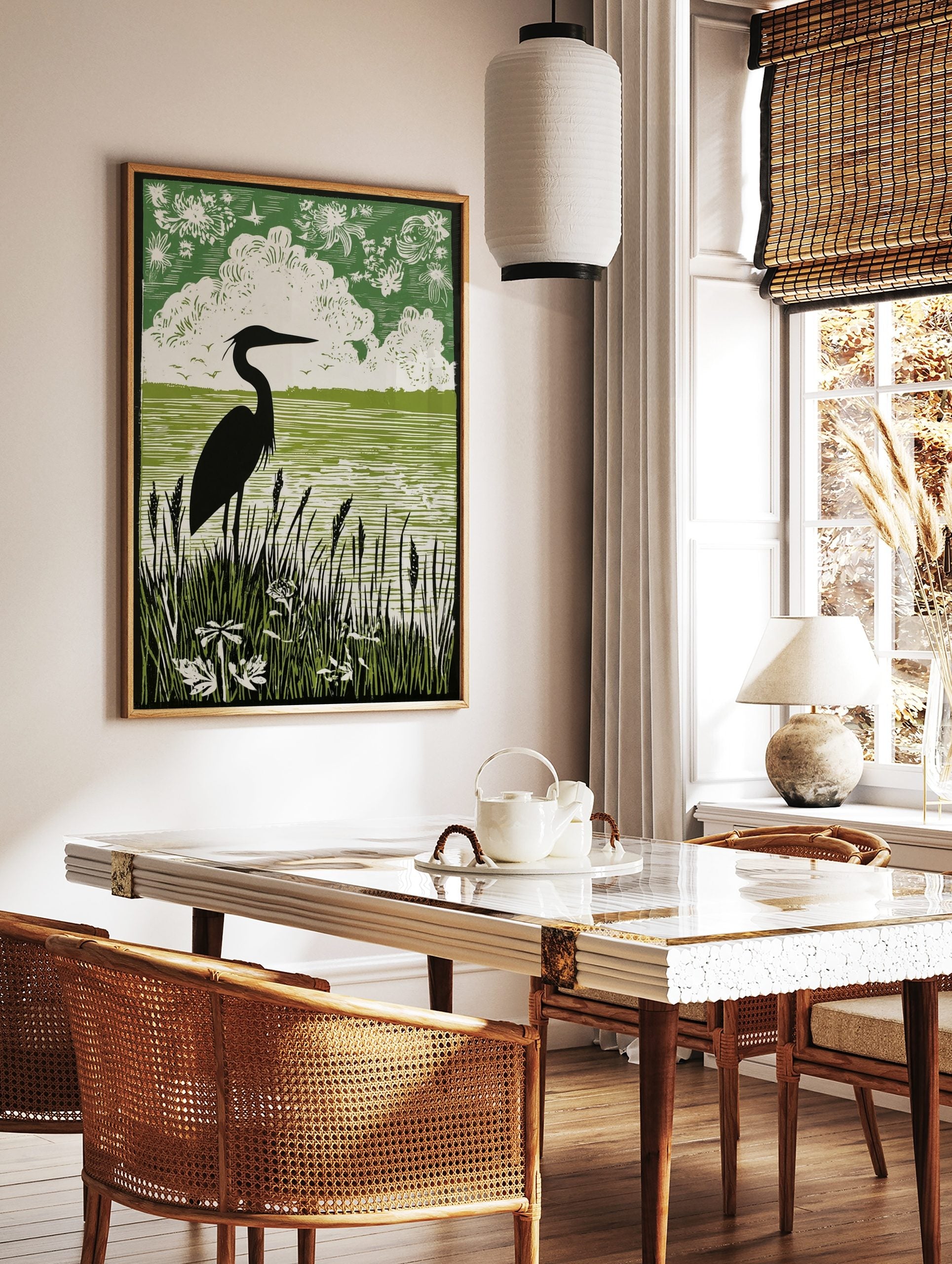 Black heron silhouette art print with green water, white clouds, and dark reeds in linocut style, in a styled room mockup