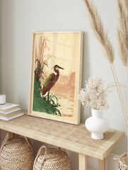 Art Nouveau style illustration of a heron standing by green reeds at a river's edge, with a, in an alternate framed mockup