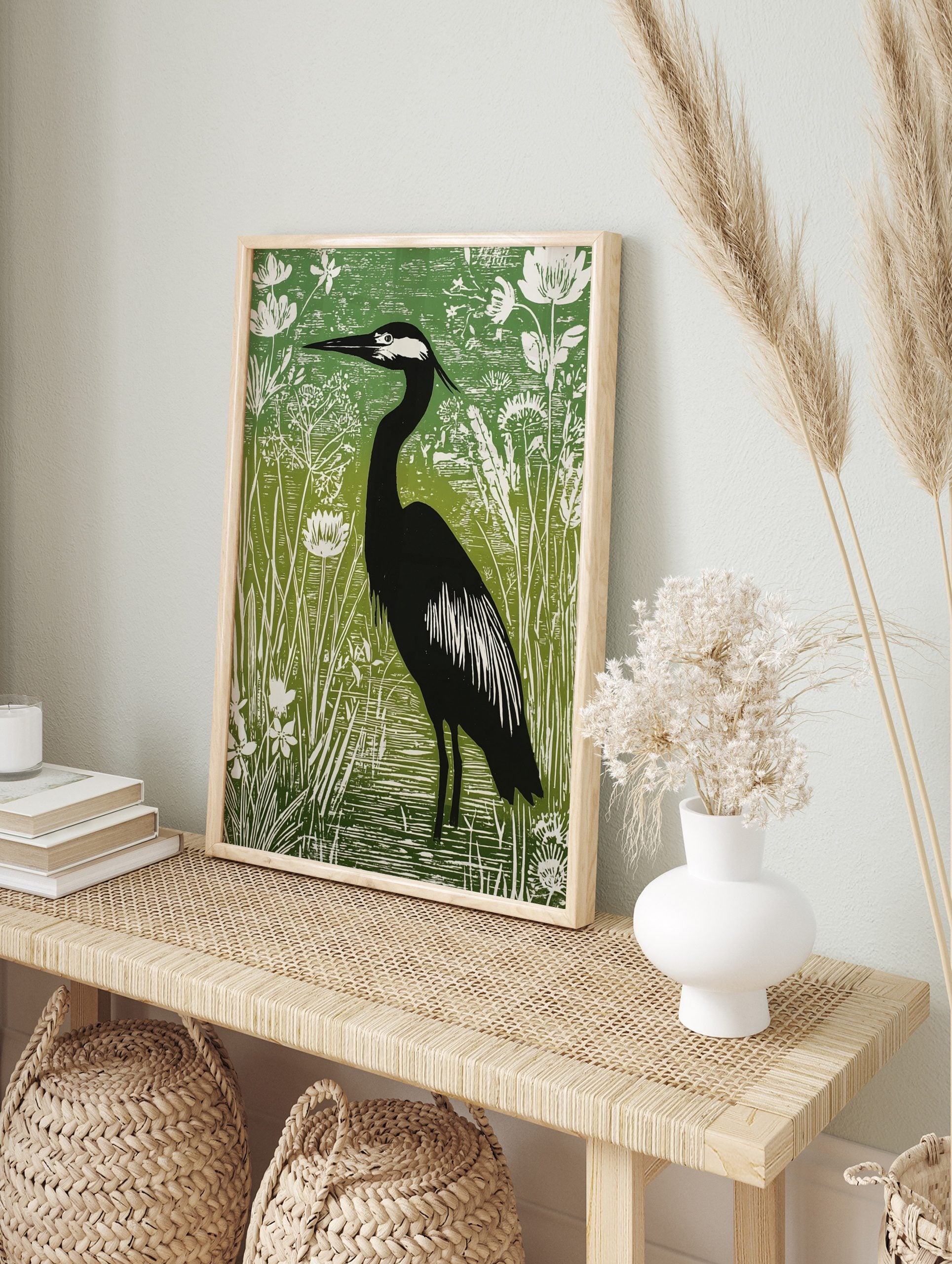 Illustrative green and black heron print standing in water amongst white botanical plants and, in an alternate framed mockup