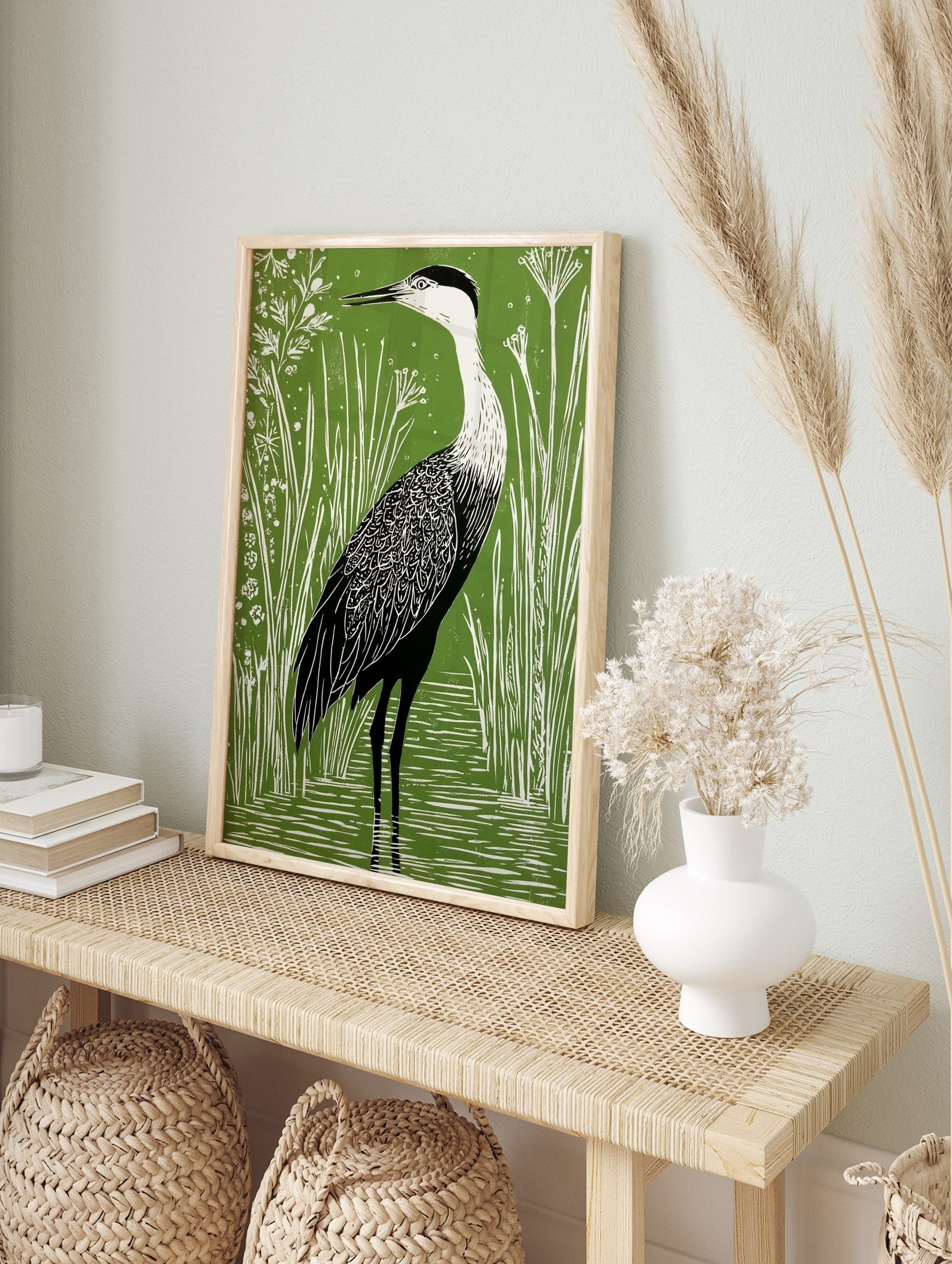 Green and white linocut style art print of a heron wading in water among tall reeds and small, in an alternate framed mockup