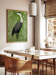 Green and white linocut style art print of a heron wading in water among tall reeds and small, in a styled room mockup