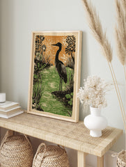Heron bird standing by rippled green water with black stylised plants and orange background, in an alternate framed mockup
