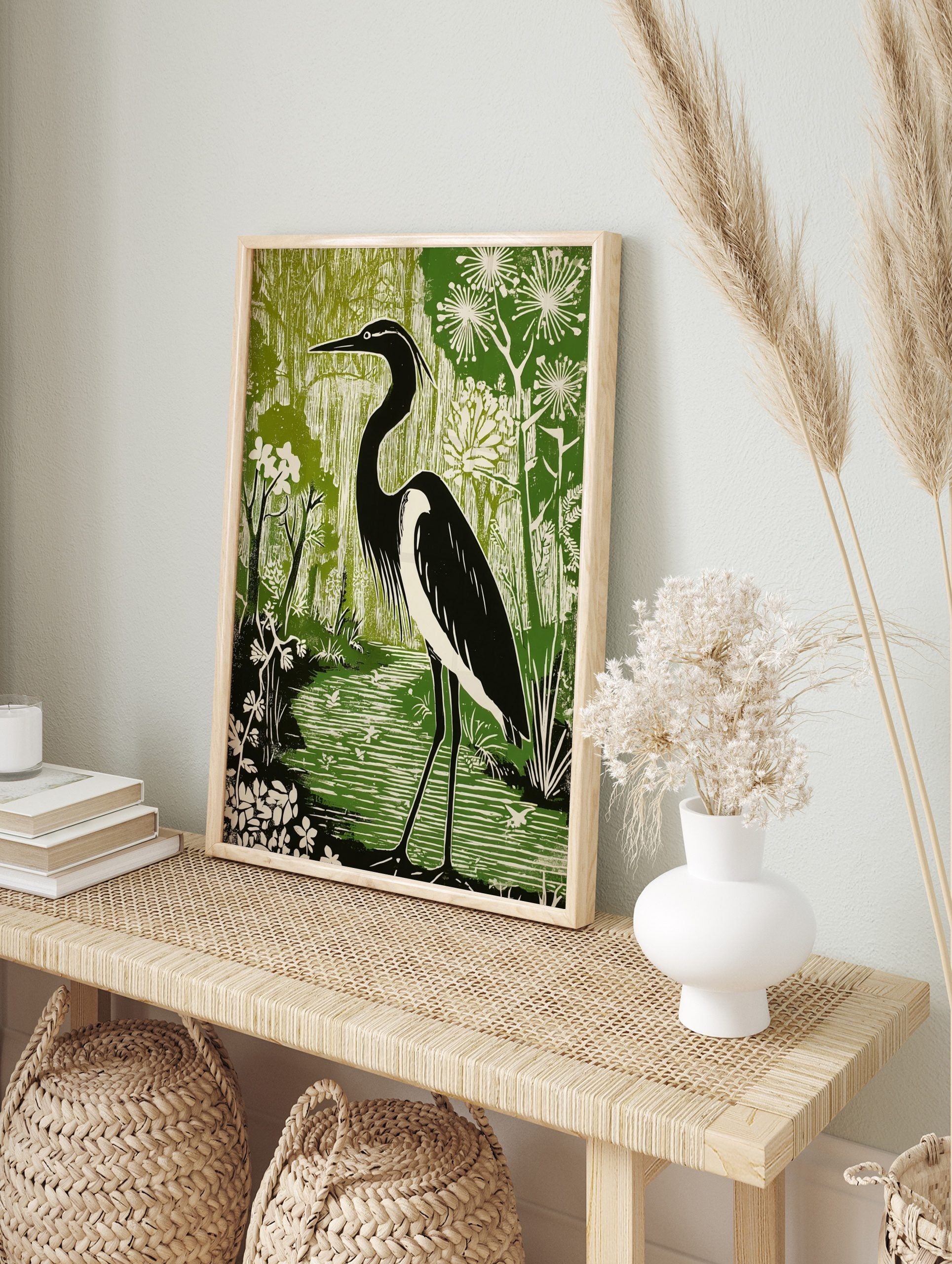 Black and white heron standing in a green wetland with flowering plants, in a linocut style, in an alternate framed mockup