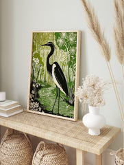Black and white heron standing in a green wetland with flowering plants, in a linocut style, in an alternate framed mockup