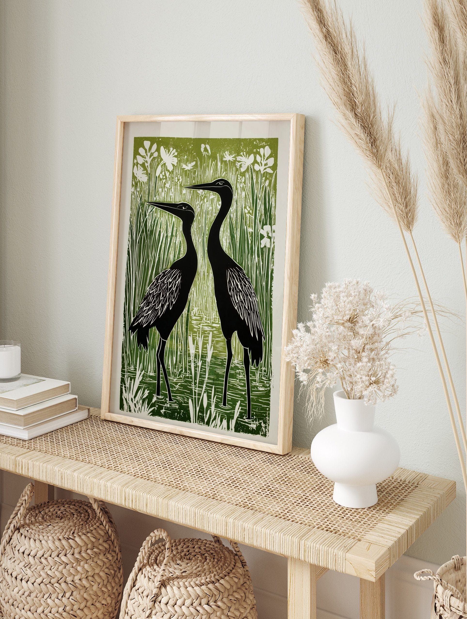 Linocut print of two black herons standing in a vibrant green wetland with white reeds and, in an alternate framed mockup