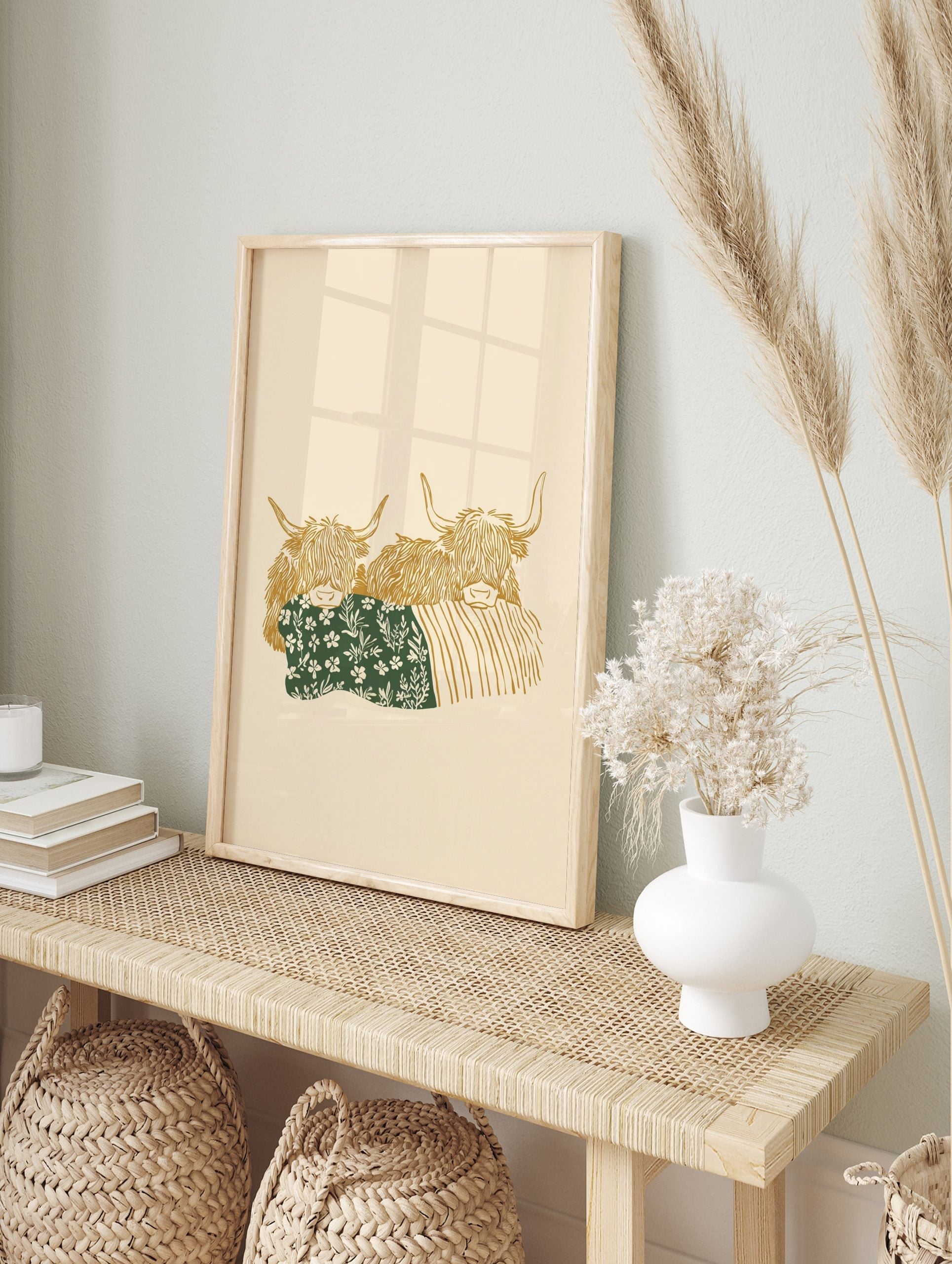 Illustrative art print of two golden Highland cows, one with a green floral blanket, on a, in an alternate framed mockup
