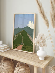 Hiker walking up a green mountain path towards a summit in a serene landscape art print, in an alternate framed mockup