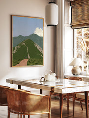 Hiker walking up a green mountain path towards a summit in a serene landscape art print, in a styled room mockup
