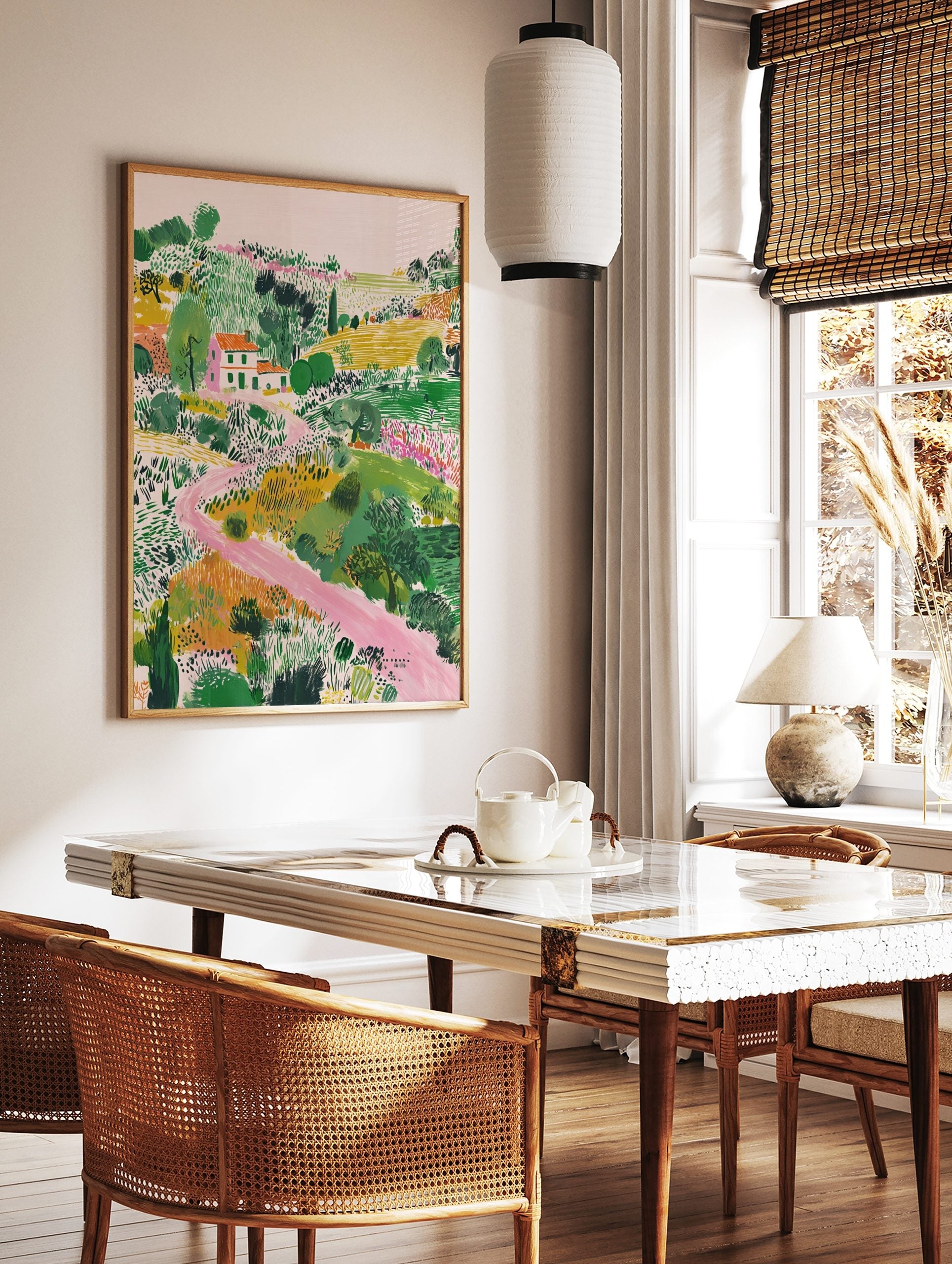 Illustrative landscape art print with a white house, orange roof, green fields, and a winding pink, in a styled room mockup
