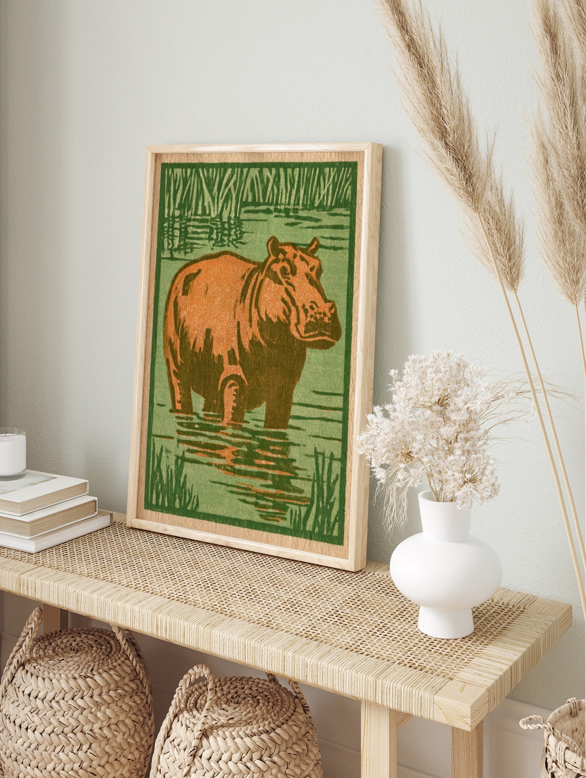 Illustrative hippo standing in water with green reeds, orange and green palette, block print, in an alternate framed mockup