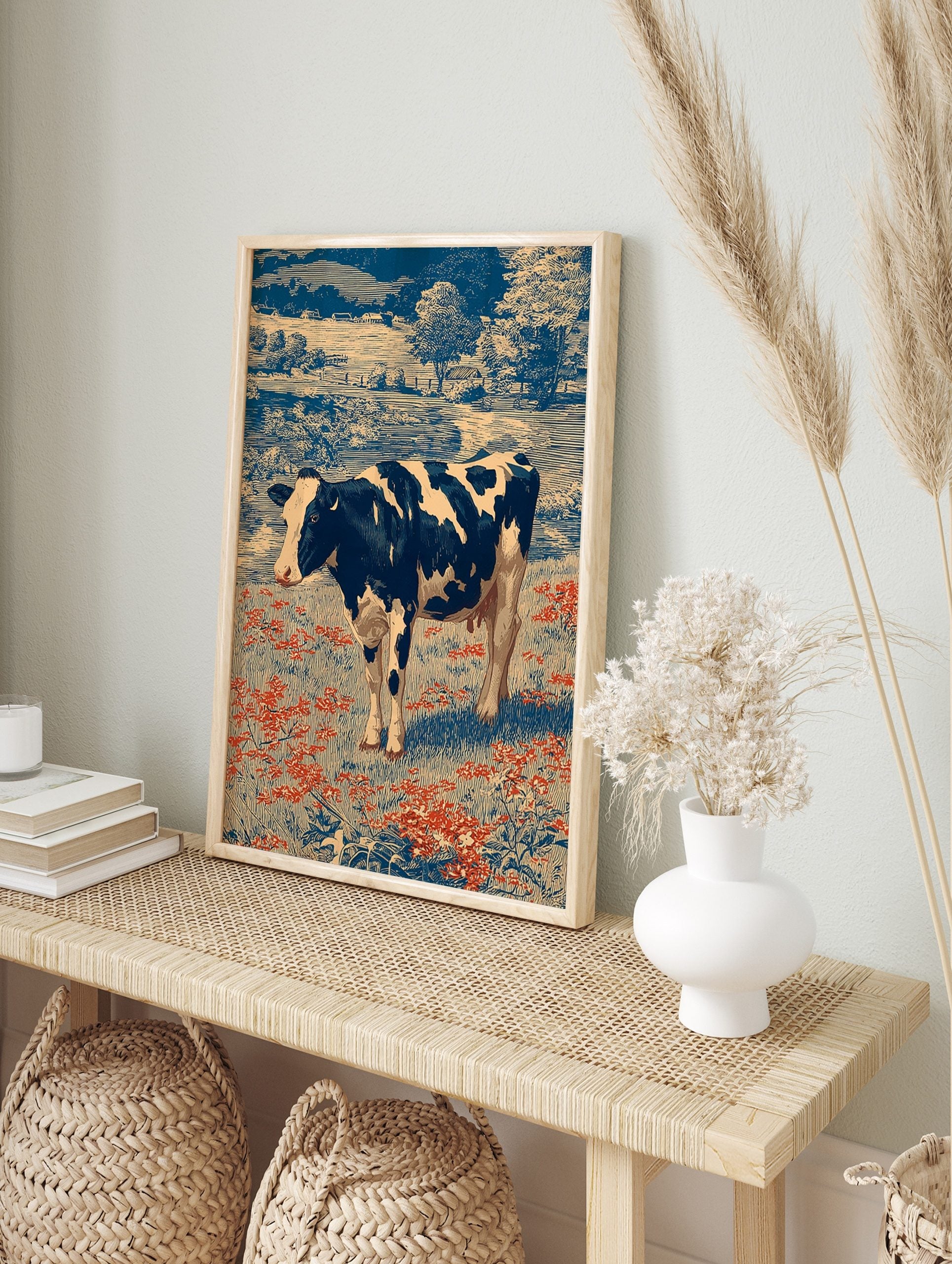 Holstein cow in a field of red flowers with blue trees and farmhouses in a vintage engraving, in an alternate framed mockup