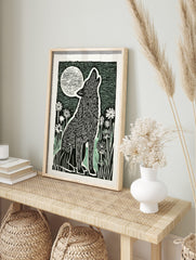 Linocut style art print of a howling wolf with a full moon and flowers in black, white, and, in an alternate framed mockup