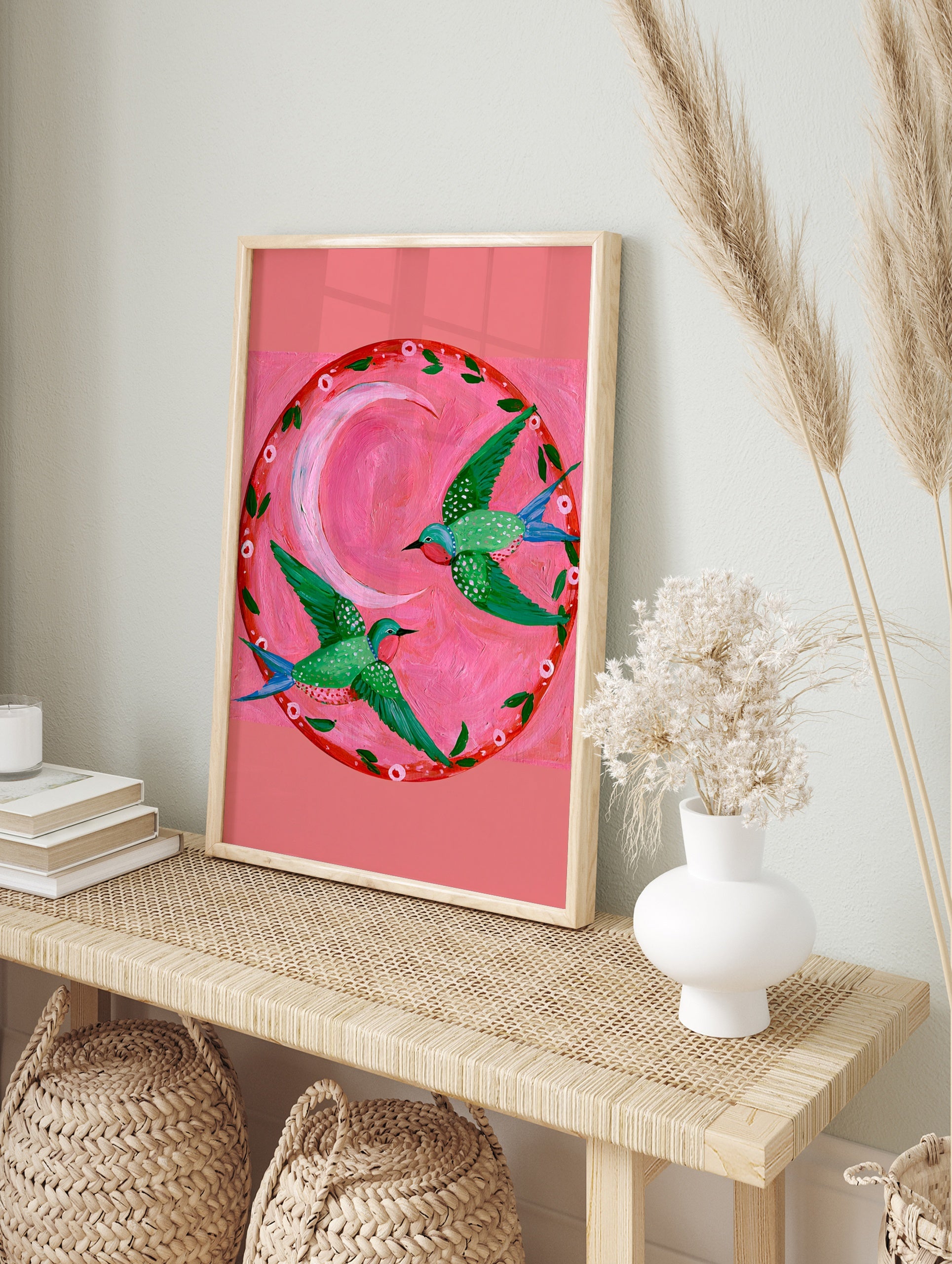 Two green hummingbirds with pink throats flying in a circle around a pink crescent moon on a, in an alternate framed mockup