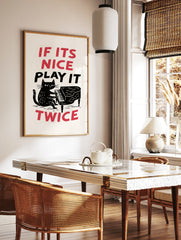 Illustration of a black cat playing a grand piano with the text If Its Nice Play It Twice in red, in a styled room mockup