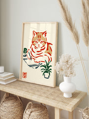 Illustrative cat writing at a desk with plants, in a Japanese woodblock print style with red, in an alternate framed mockup