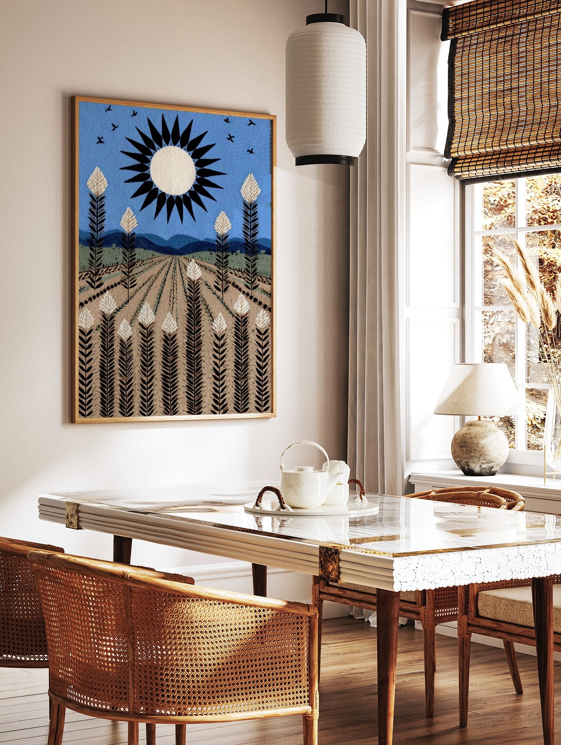 Illustrative field landscape art print with black sun, white-topped crops, blue sky, and mountains, in a styled room mockup