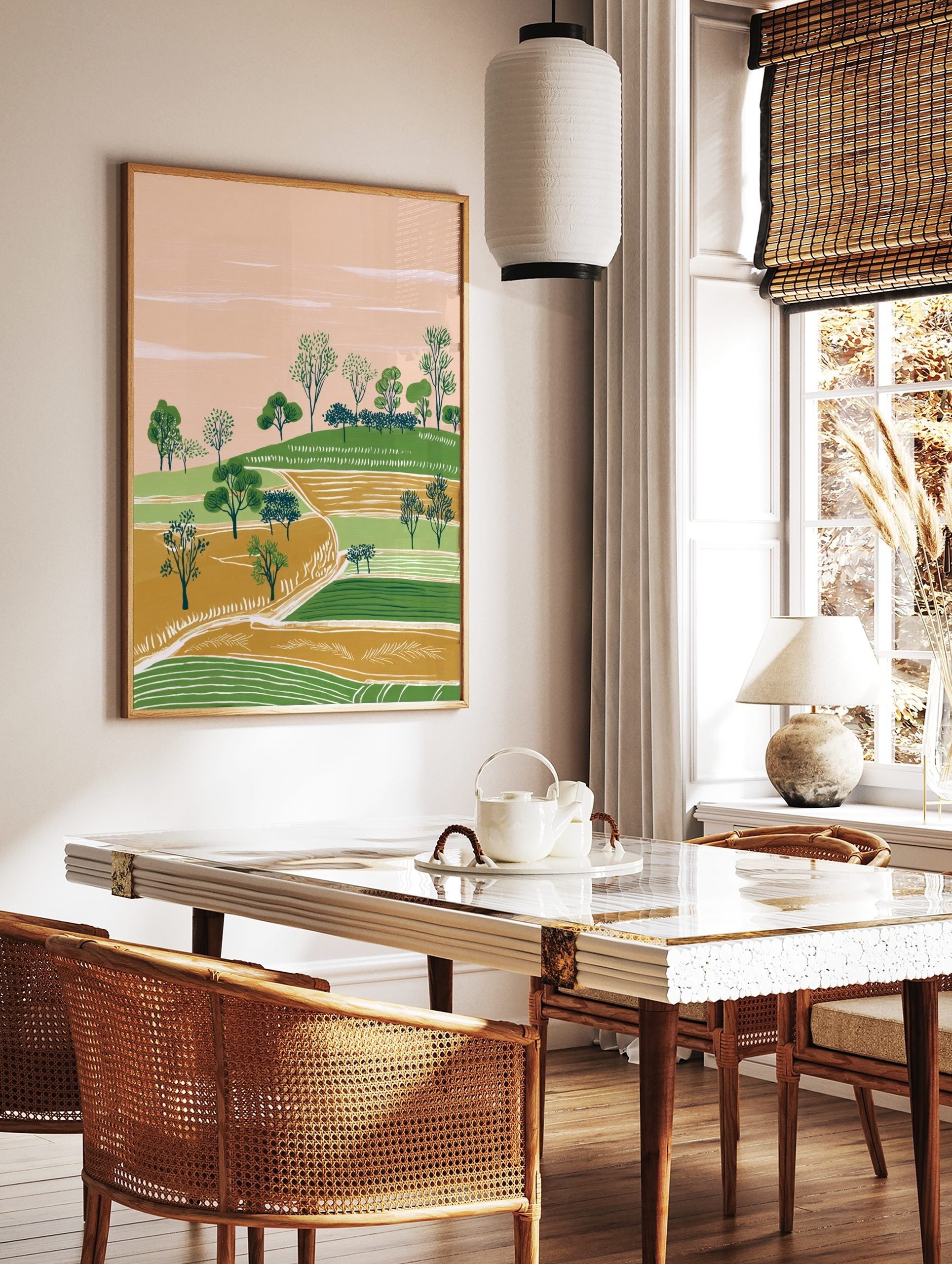 Illustrative landscape art print with green hills, gold fields, scattered trees, and a peach sky, in a styled room mockup