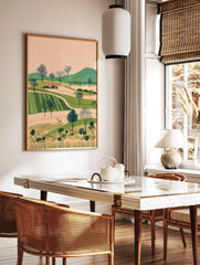 Illustrative landscape art print with rolling green hills, cultivated fields, and dotted trees, in a styled room mockup