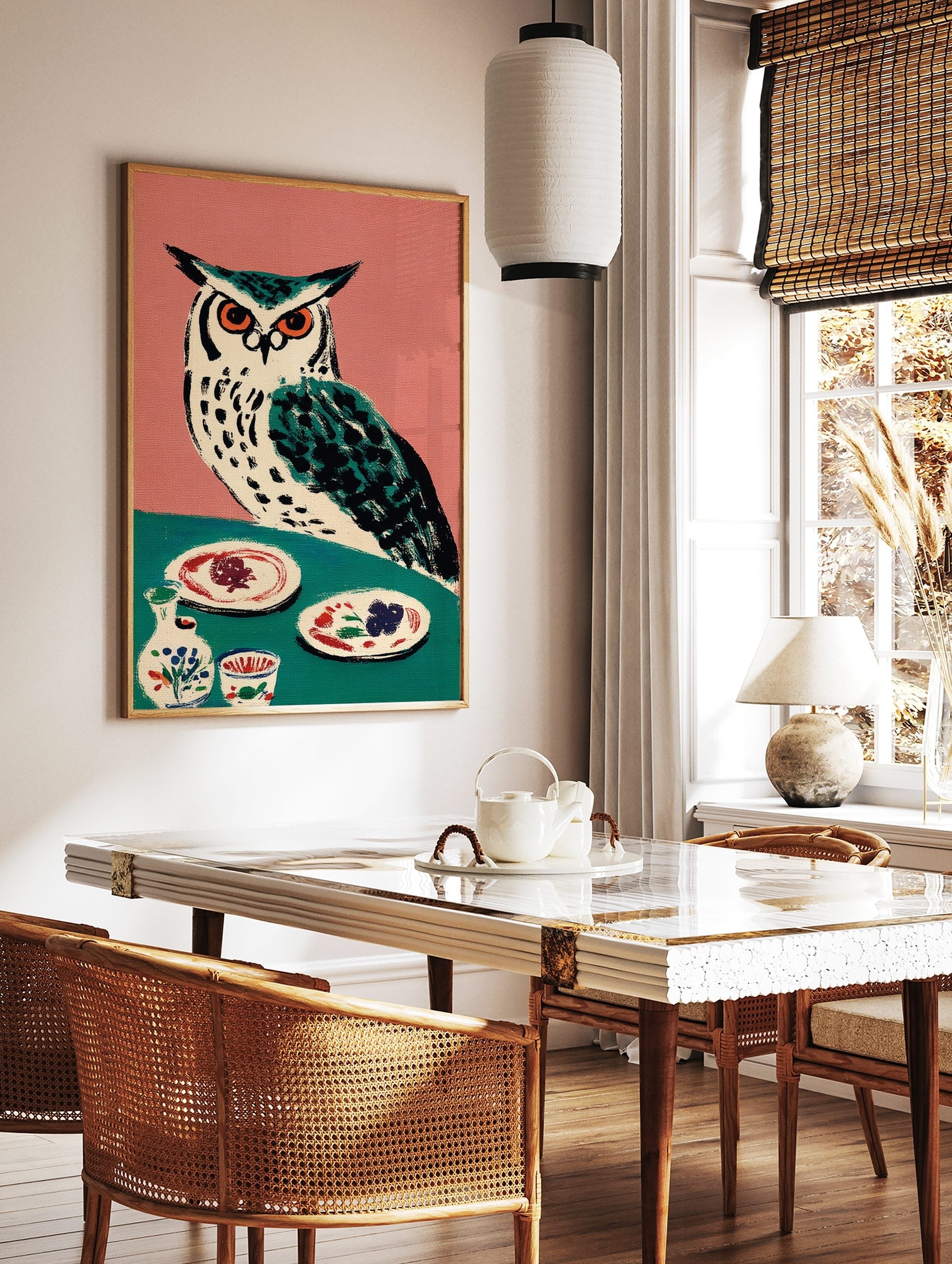 Illustrative owl with orange eyes on teal table with plates and pottery, pink background, folk art, in a styled room mockup