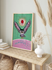 Illustrative owl with spread wings, red sun, and pink landscape on green background wall art, in an alternate framed mockup