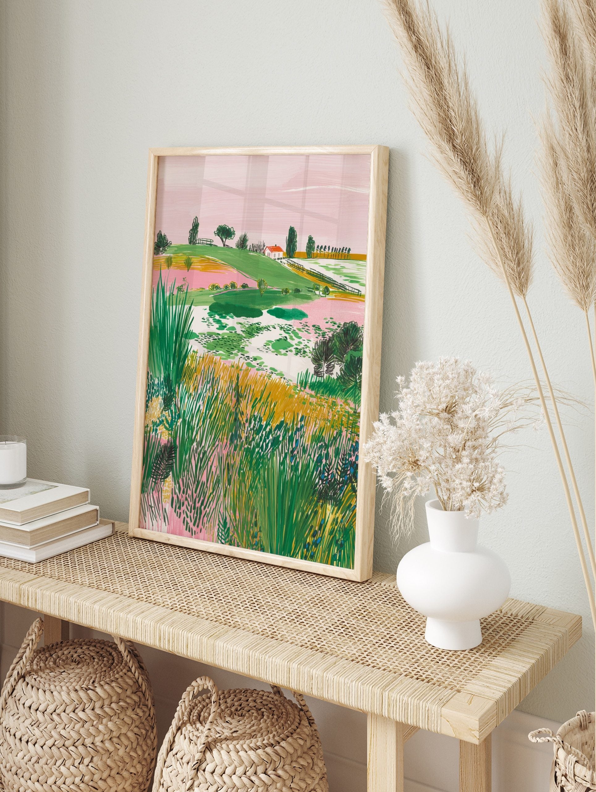 Illustrative landscape art print with green hills, pink sky, a red-roof house, and foreground, in an alternate framed mockup