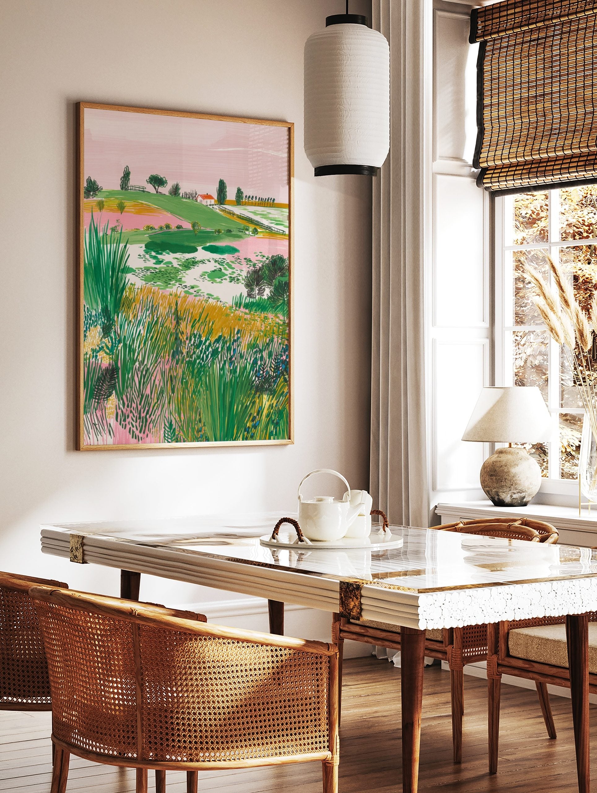Illustrative landscape art print with green hills, pink sky, a red-roof house, and foreground, in a styled room mockup