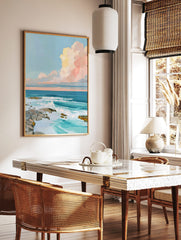 Impressionistic ocean wall art with crashing waves, rocky shore, and pastel pink and yellow clouds, in a styled room mockup