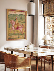 Indian miniature painting of a bearded man in a pink turban riding an ornate pink horse in a green, in a styled room mockup