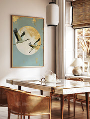 Japanese crane wall art with two birds in flight against a large textured gold sun on a pale blue, in a styled room mockup