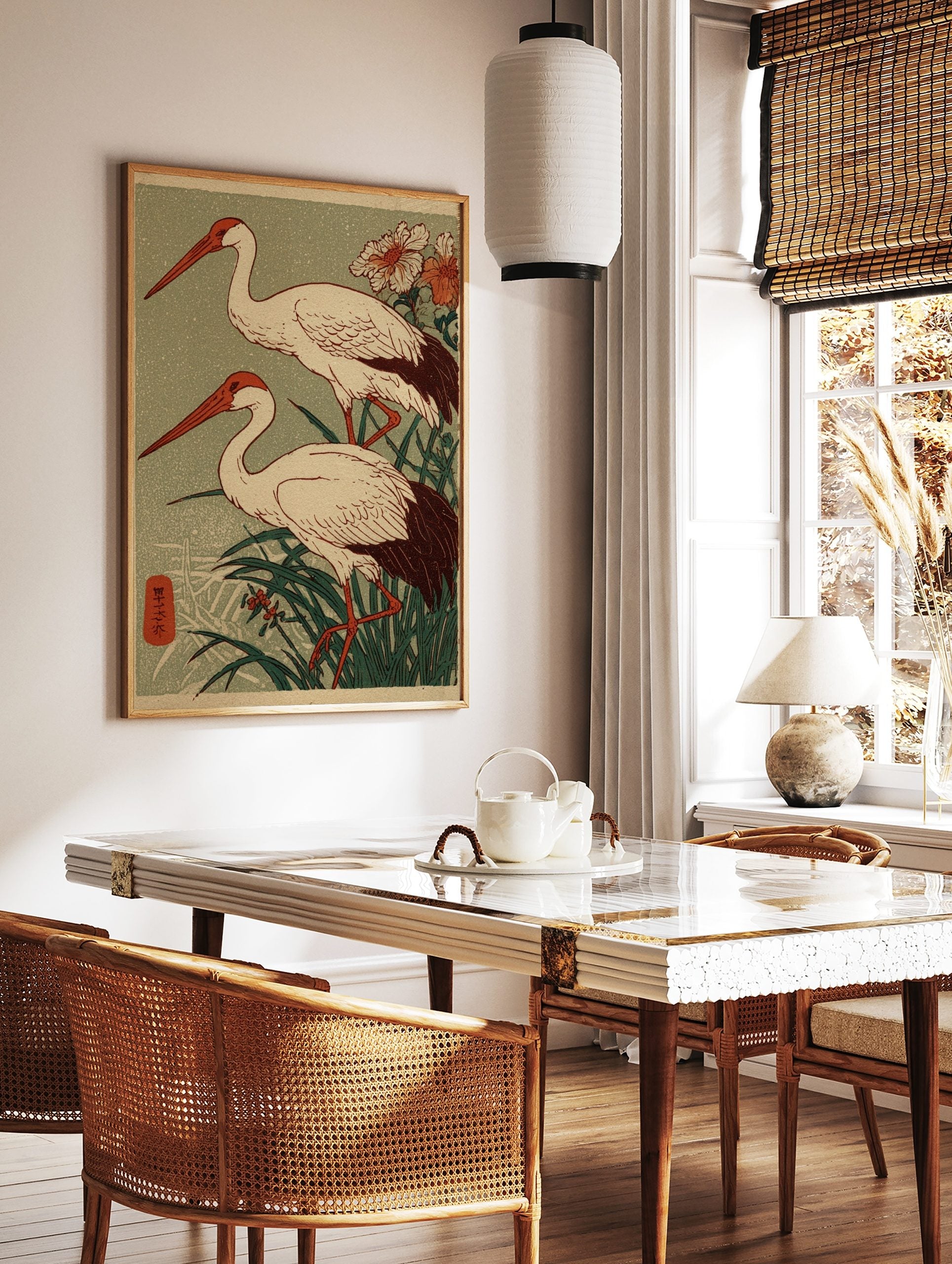 Two Japanese cranes with red beaks and dark tails stand in green reeds, woodblock print style, in a styled room mockup