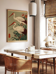 Two Japanese cranes with red beaks and dark tails stand in green reeds, woodblock print style, in a styled room mockup