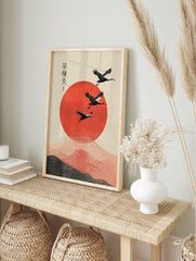 Three black cranes fly over a large textured red sun with wavy lines and Japanese calligraphy, in an alternate framed mockup