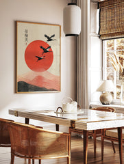Three black cranes fly over a large textured red sun with wavy lines and Japanese calligraphy on a, in a styled room mockup