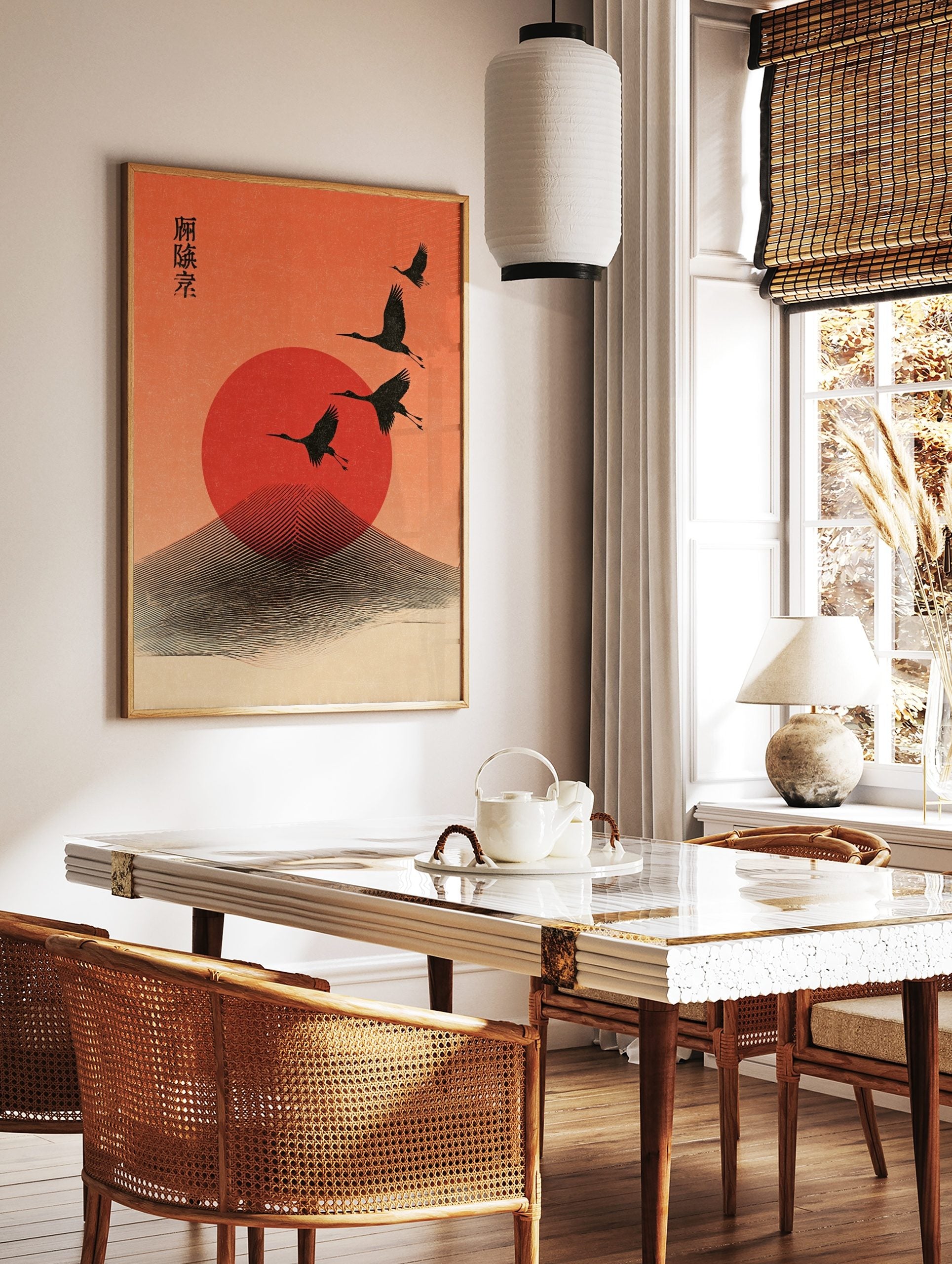 Four black cranes flying across a red sun and stylised mountain against an orange sky, with, in a styled room mockup