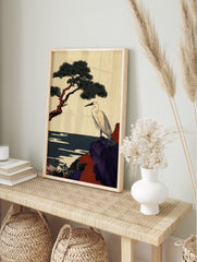 Japanese egret stands on a purple and red rocky cliff with a pine tree and dark blue sea, in an alternate framed mockup