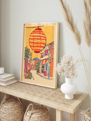 Illustrative print of a Japanese street scene with a large orange striped lantern hanging above colorful buildings and trees. - Image 3