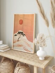 Japanese-style illustration of a pine tree on a hillside with a large red sun in an orange sky, in an alternate framed mockup