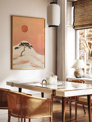 Japanese-style illustration of a pine tree on a hillside with a large red sun in an orange sky, in a styled room mockup