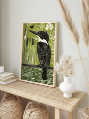 Linocut-style print of a black and white kingfisher bird on a branch over green water with, in an alternate framed mockup