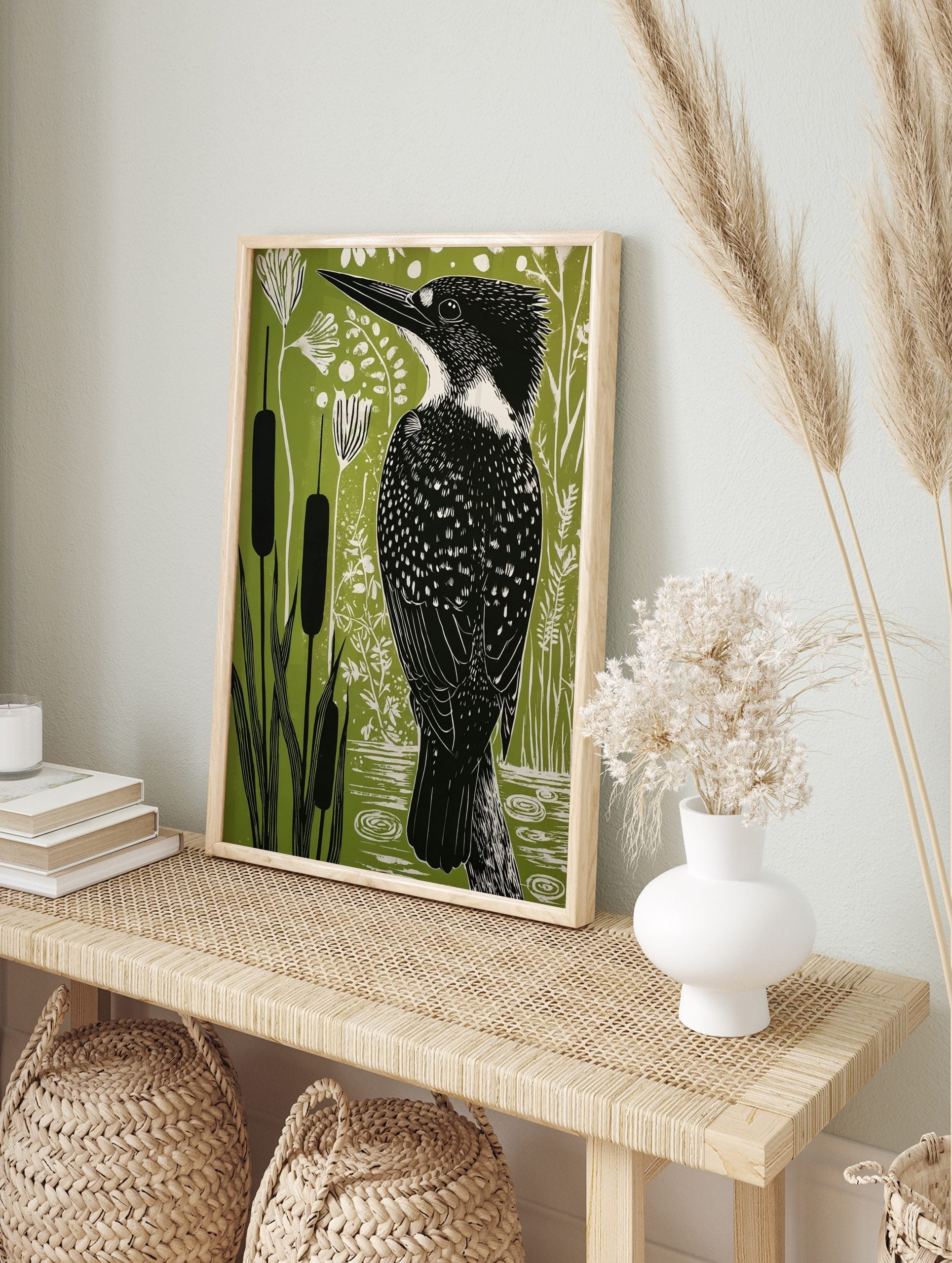 Illustrative linocut style print of a kingfisher bird among cattails and plants on a green, in an alternate framed mockup