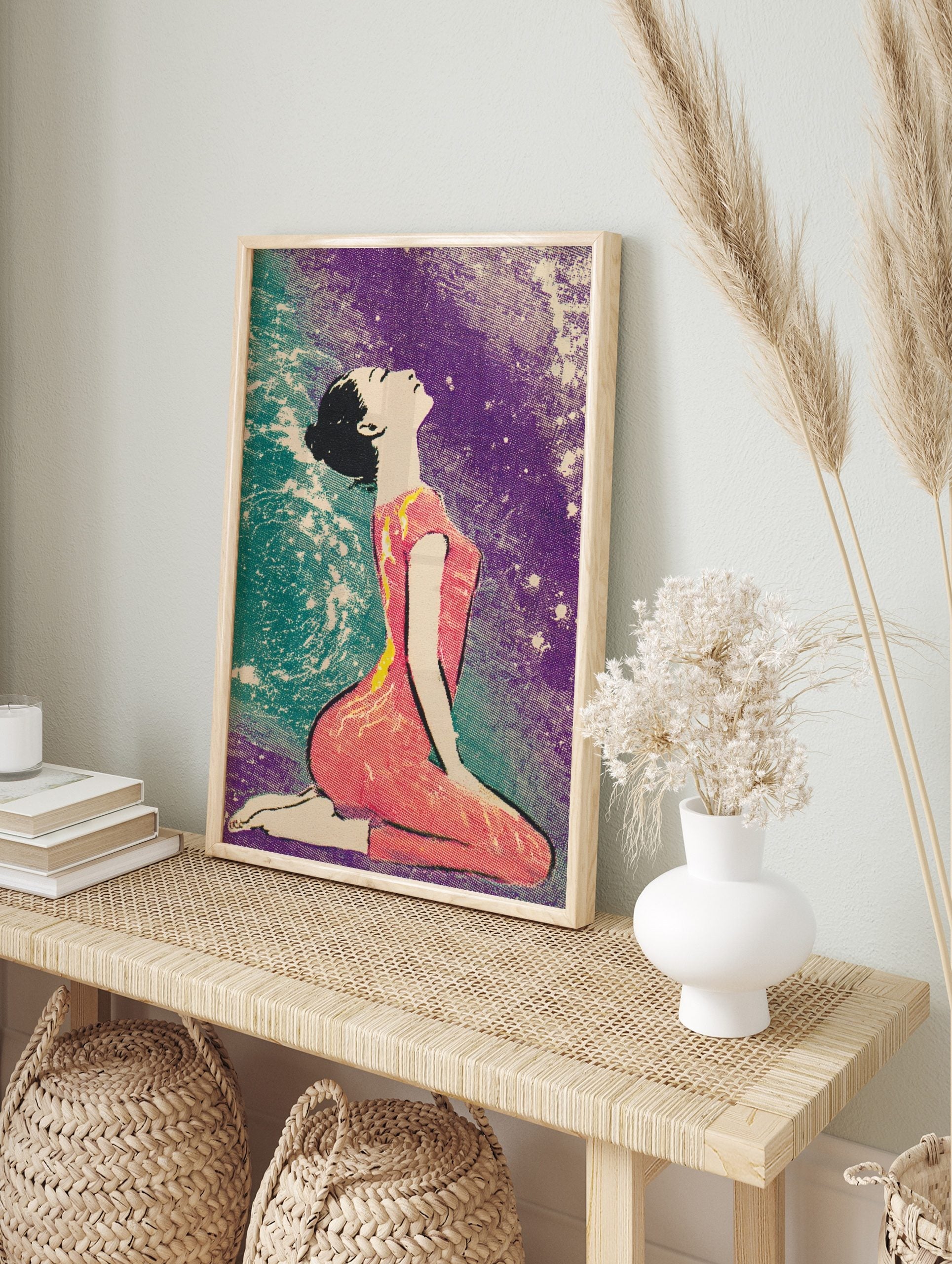 Illustrative print of a woman kneeling, looking up, with a pink outfit and a purple and teal, in an alternate framed mockup