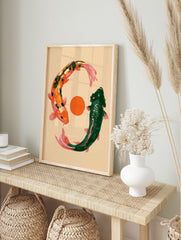 Illustrative art print of two koi fish, one orange and one green, circling an orange sun on a, in an alternate framed mockup
