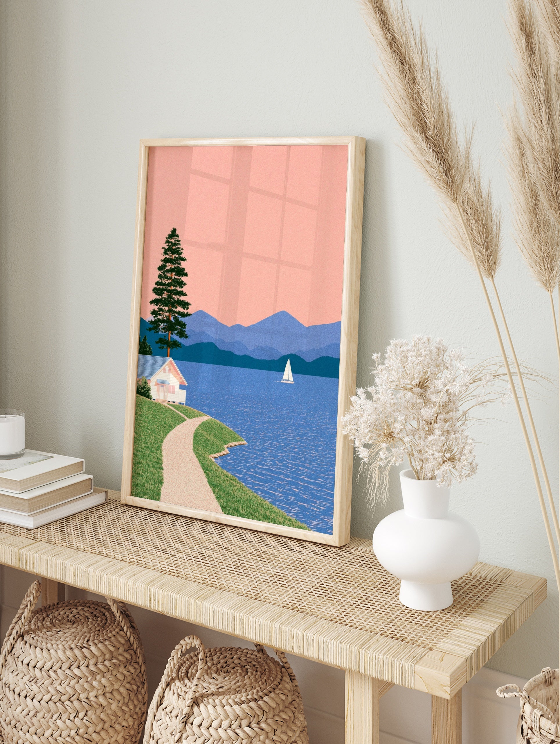 Illustrative lakeside landscape with a white cottage, pine tree, sailboat, and blue mountains, in an alternate framed mockup