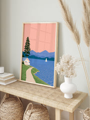 Illustrative lakeside landscape with a white cottage, pine tree, sailboat, and blue mountains, in an alternate framed mockup