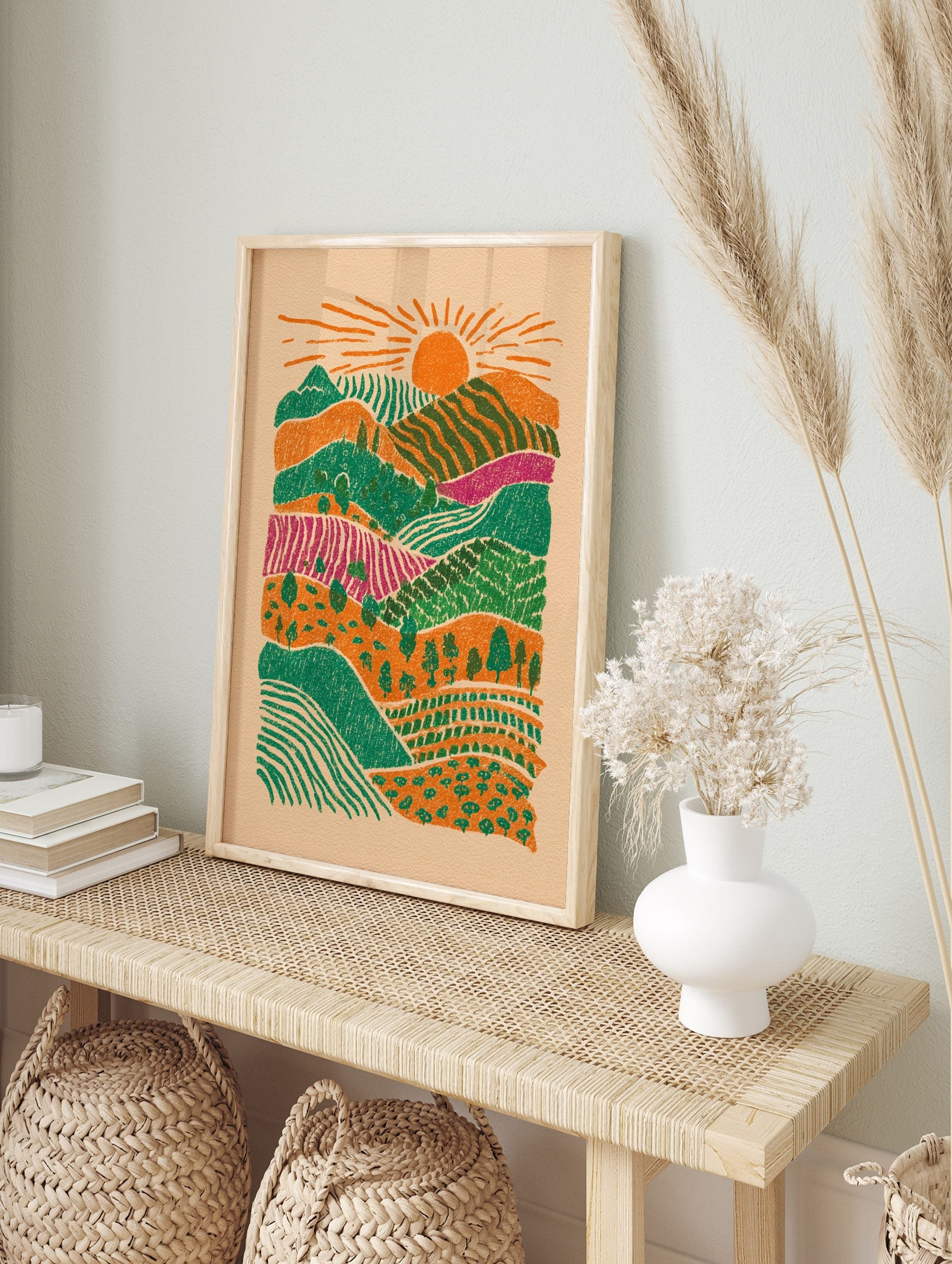 Illustrative layered landscape art print with orange sun, green hills, magenta fields, and, in an alternate framed mockup