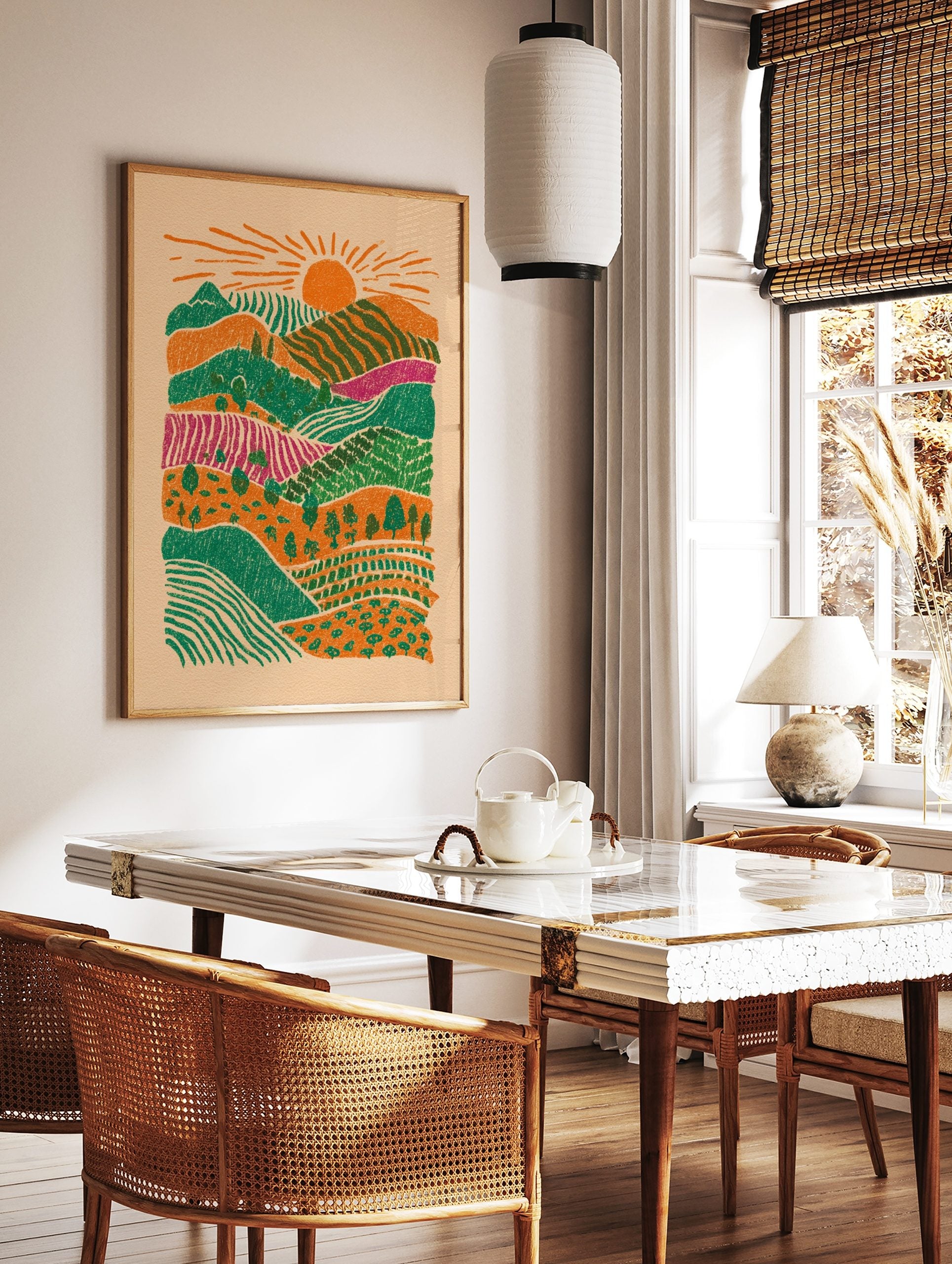 Illustrative layered landscape art print with orange sun, green hills, magenta fields, and trees, in a styled room mockup