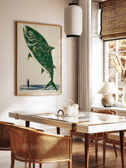 Illustrative print of a large green fish leaping from blue water, with a small fisherman holding a, in a styled room mockup