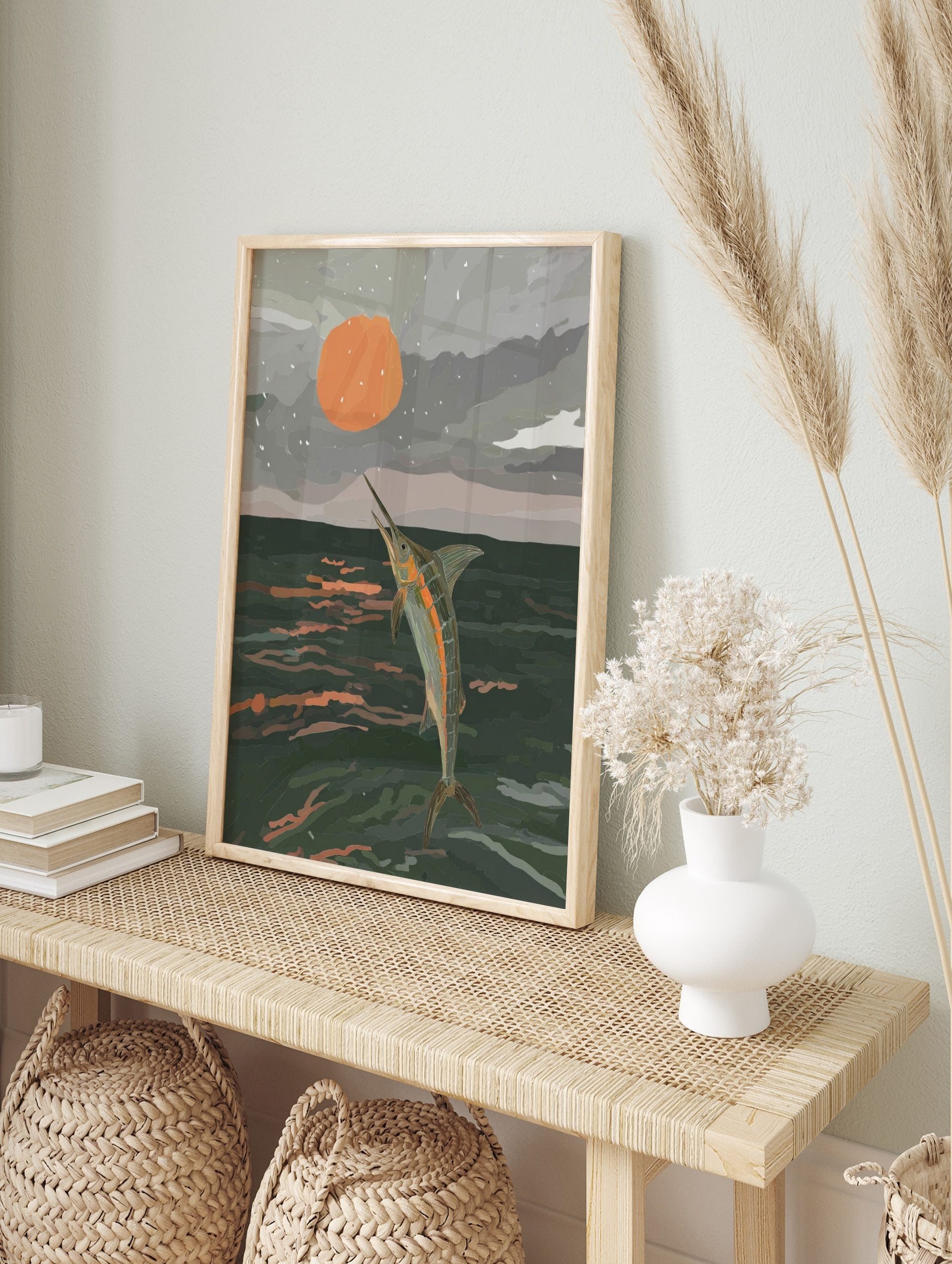 Illustrative print of a marlin leaping from dark ocean water towards a large orange sun in a, in an alternate framed mockup